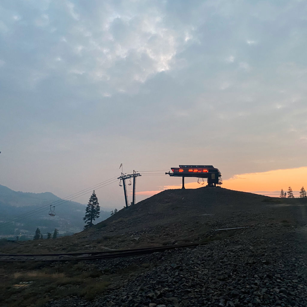 Ski lift at the top of a hill with internal red lights, backdrop is cloudy, hazy sunrise